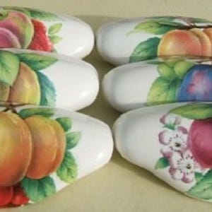 May include: Six white ceramic drawer pulls with a fruit design. Each pull features a different fruit arrangement, including peaches, plums, and berries.