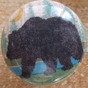 May include: A round ceramic knob with a black bear silhouette against a blue lake and green forest background. The knob has a glossy finish and a light brown crescent moon in the upper left corner.