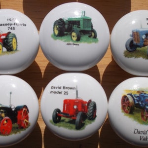 May include: Six round ceramic knobs with images of vintage tractors. The knobs feature different tractor models, including a red Massey-Harris 745, a green John Deere, a blue Ferguson model 35, a red David Brown model 25, a blue David Brown Vak IC, and a gray Fordson model F.