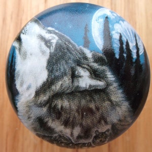 May include: Round button with a wolf howling at the moon. The button features a detailed illustration of a gray and white wolf against a blue night sky with a full moon and silhouetted trees.