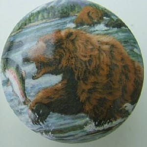 May include: A brown bear with its mouth open is catching a salmon in a river. The bear is in the water and the salmon is jumping out of the water. The background is a forest and a river.
