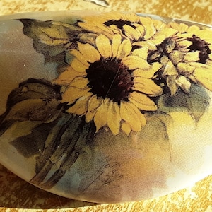 May include: A white ceramic stone with a painted design of sunflowers in shades of yellow, brown, and green.