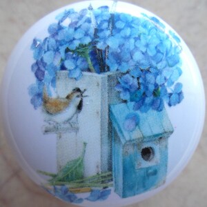 May include: A white ceramic knob with a bluebird perched on a branch, a blue birdhouse, and a bouquet of blue flowers.