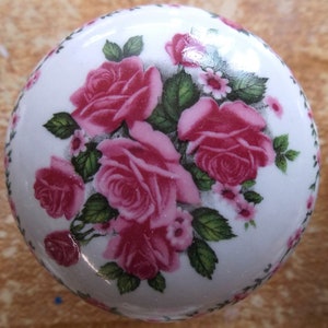 May include: White ceramic knob with a floral design featuring pink roses and green leaves.