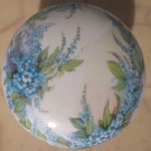 May include: A white ceramic knob with a floral design featuring blue and green forget-me-not flowers.
