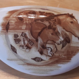 May include: White ceramic oval dish with a brown design of three horses running in a circle. The horses are brown and white and have a stylized design. The background is a light brown with a stylized design.