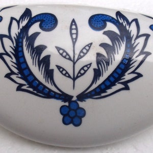 May include: A white ceramic dish with a blue and black floral design. The dish is oval shaped and has a smooth, glossy finish.
