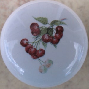May include: A white ceramic knob with a red and green cherry design.
