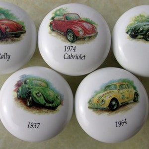 May include: Five white ceramic knobs with different vintage Volkswagen Beetle designs. Each knob features a different year and model of the car, including 1973 Rally, 1974 Cabriolet, 1946, 1937, and 1964.