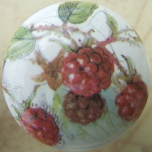May include: White ceramic knob with a floral design featuring red and green raspberries. The knob has a smooth, glossy finish.