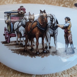 May include: White ceramic decorative piece with a detailed illustration of a horse-drawn carriage. The image features a brown and white horse team, a driver, and a man. The piece has a smooth, curved shape.