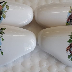 May include: Set of four white ceramic drawer pulls with birdhouse and bird designs. Each pull features a different birdhouse with a bird perched on the edge. The birdhouses are painted in shades of brown, green, and blue.