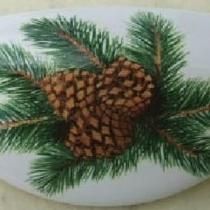 May include: A white ceramic oval dish with a painted design of pine branches and pine cones. The pine cones are brown and the pine branches are green.