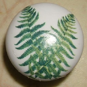 May include: White ceramic cabinet knob featuring a detailed green fern leaf design. The knob is round and has a glossy finish. The fern leaves are arranged in a symmetrical pattern, adding a touch of nature-inspired decor.
