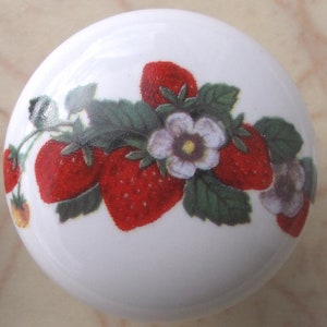 May include: White ceramic knob with a red and green strawberry design. The knob features a cluster of strawberries with leaves and white flowers.