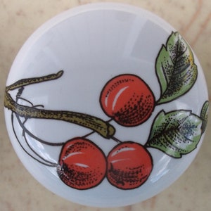 May include: White ceramic knob with a red cherry branch design. The knob features three red cherries with green leaves on a white background.