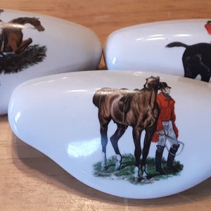 May include: Three white ceramic drawer pulls with a horse and rider design. Each pull features a different horse and rider in a red jacket. The horses are brown, black, and a light brown color.