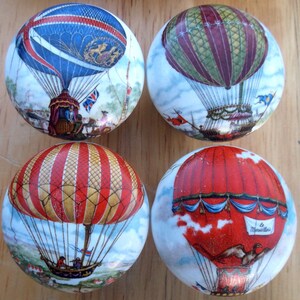 May include: Four decorative cabinet knobs with hot air balloon designs. Each knob features a different balloon, with colors including red, blue, and gold. The knobs have a round shape and are likely made of ceramic or porcelain.