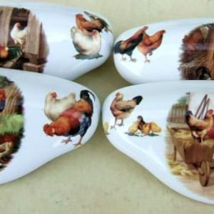 May include: Four white, oval-shaped ceramic serving dishes. Each dish features a different pastoral scene with chickens and roosters in a farm setting. The artwork includes various colors, such as brown, red, and green.