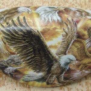 May include: A white ceramic oval-shaped ornament with a colorful image of multiple bald eagles in flight against a sunset background.