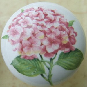 May include: A white ceramic knob with a pink hydrangea flower design. The flower is painted in shades of pink and white with green leaves.