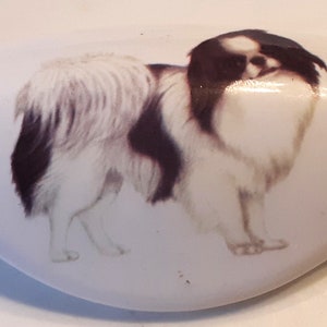 May include: A white ceramic dish with a black and white illustration of a Japanese Chin dog. The dog is standing on all four paws with its tail curled up.
