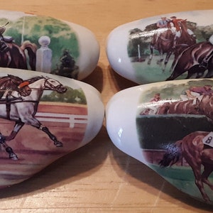 May include: Four white, oval-shaped drawer pulls with horse racing scenes. Each pull features a different image of jockeys on horseback, with vibrant colors and detailed depictions of the horses and the race track.