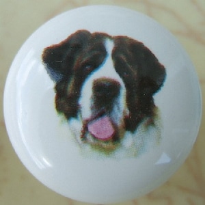 May include: A white ceramic knob with a brown and white dog printed on it. The dog has a pink tongue sticking out.