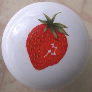 May include: A white ceramic knob with a red and green strawberry design.