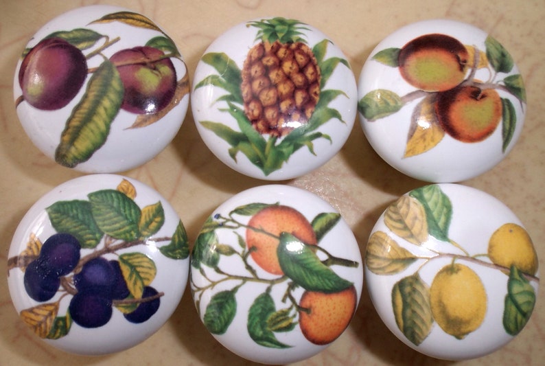 May include: Six white ceramic knobs with different fruit designs. The knobs feature a pineapple, plums, lemons, oranges, and apples.