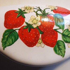 May include: White ceramic door handle with a painted design of ripe red strawberries, green leaves, and small white flowers. The handle has a smooth, curved shape, and the strawberry design is centered on the handle.