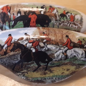 May include: Two ceramic door knobs with a hunting scene. The knobs are white with a brown, green, and red design. The scene depicts riders on horseback in a forest.