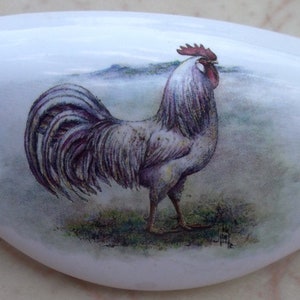 May include: A white ceramic rooster figurine with a red comb and wattle. The rooster is standing on a green and brown background.