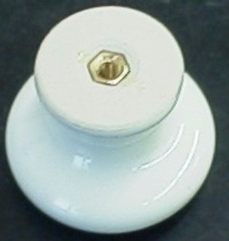 May include: White ceramic knob with a gold screw hole in the center. The knob has a rounded top and a flared base.