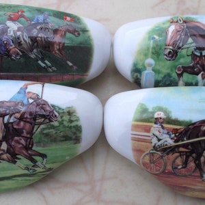 May include: Four white, oval-shaped decorative stones. Each stone features a different equestrian scene: horse racing, show jumping, and harness racing. The scenes are painted with vibrant colors, depicting jockeys and horses in action. The stones are ideal for home decor.