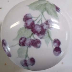 May include: White ceramic knob with a design of purple berries and green leaves.