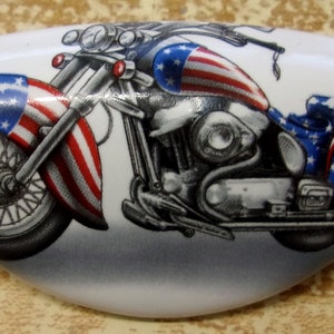 May include: A white ceramic cabinet knob with a colorful image of a motorcycle with an American flag design. The motorcycle is a cruiser style with a large front wheel and a sidecar.