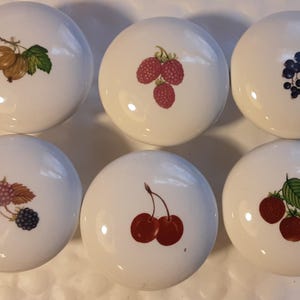May include: Six white ceramic knobs with different fruit designs. Each knob features a single fruit or berry, including cherries, raspberries, gooseberries, blackberries, and strawberries.