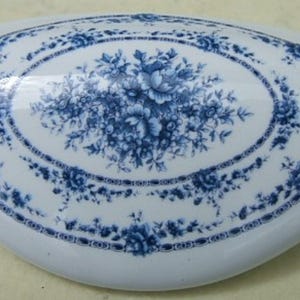 May include: White ceramic soap dish with a blue floral design. The oval-shaped dish features a central bouquet and a border of delicate blue flowers and leaves. A classic, decorative bathroom accessory.