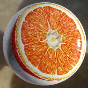 May include: A close-up of a ceramic orange with a detailed image of a sliced orange on the front. The orange is a bright orange color with a white background.