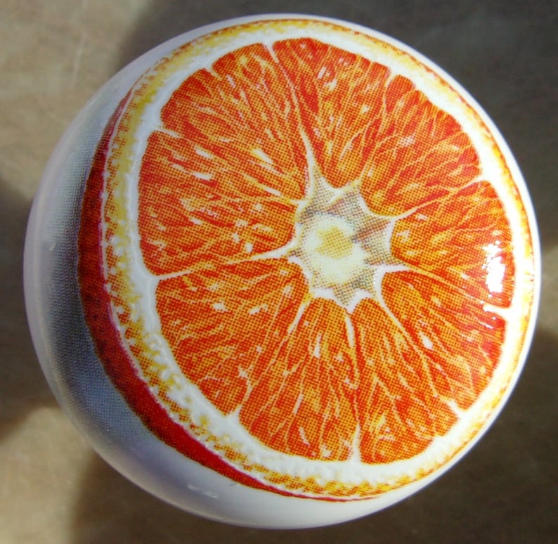 May include: A close-up of a ceramic orange with a detailed image of a sliced orange on the front. The orange is a bright orange color with a white background.