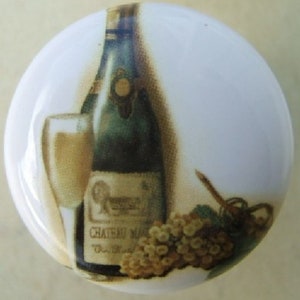 May include: White ceramic cabinet knob featuring a wine bottle, a filled wine glass, and a bunch of grapes. The bottle has a label that reads "Chateau Mas". The image has a vintage, classic style.