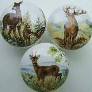 May include: Three round decorative cabinet knobs with deer illustrations. Each knob features a different deer scene, with varying colors and backgrounds. The knobs are likely made of ceramic or porcelain and are suitable for furniture or cabinet upgrades.