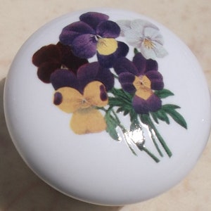 May include: A white ceramic knob with a floral design featuring purple, yellow, and white pansies.
