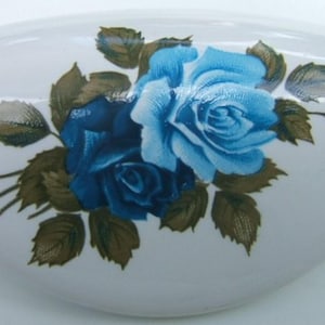 May include: White, oval-shaped ceramic dish decorated with blue roses and green leaves. The roses are in various stages of bloom, with a detailed floral design. A decorative piece for the home.