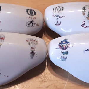 May include: Set of four white ceramic drawer pulls with a hot air balloon design. Each pull features a different colored balloon with various details, including stripes, stars, and floral patterns.