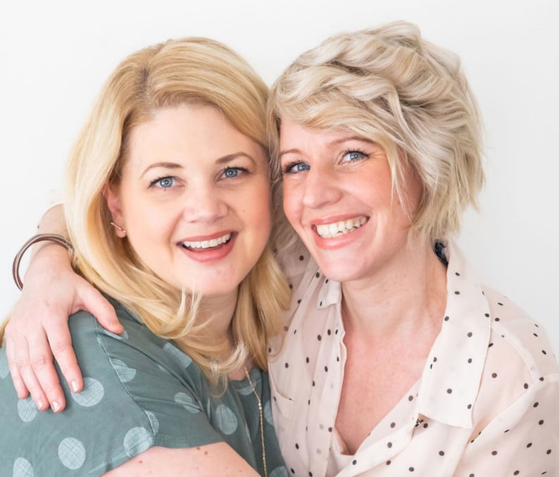 May include: Two women with blonde hair are smiling and hugging. They are both wearing polka dot shirts. The woman on the left is wearing a green shirt and the woman on the right is wearing a white shirt.