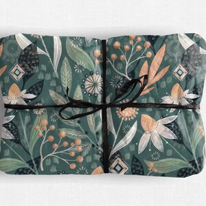 May include: Gift-wrapped package with a dark teal floral pattern featuring white, orange, and green botanical elements. The package is tied with a black ribbon. The design includes stylized flowers, leaves, and berries.