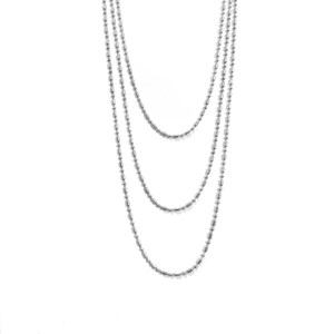 Puede incluir: Collar plateado de tres hilos. Cada hilo está compuesto por pequeñas cuentas alargadas. El collar cuelga sobre un fondo blanco, con los hilos cayendo en cascada hacia abajo, creando un efecto de capas. Las cuentas reflejan la luz.