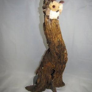 May include: A whimsical owl sculpture made from natural driftwood and other materials. The owl has a white body with brown accents and a large, round head.